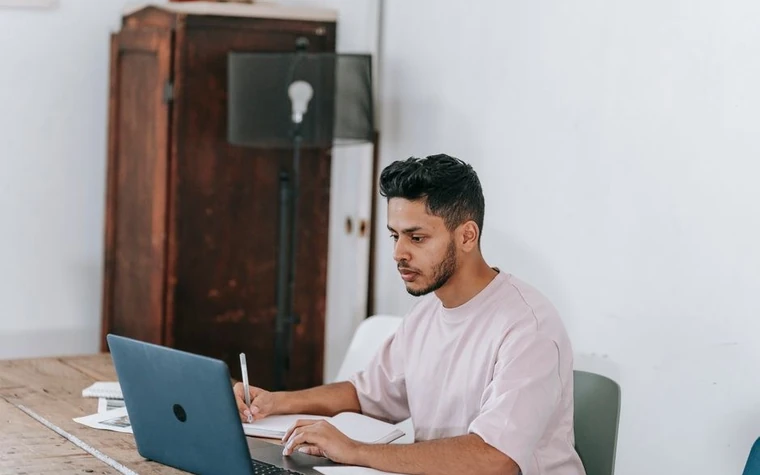 Man at a home desk concentrating on a laptop screen
