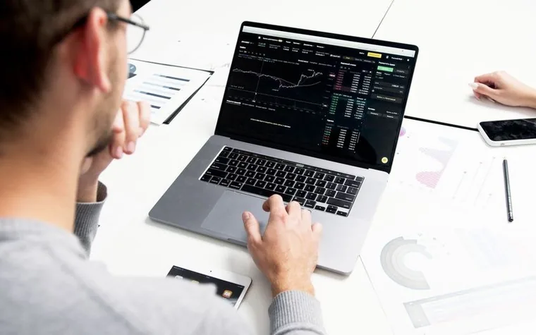 Man in a dark shirt reviewing betting data across two laptop screens