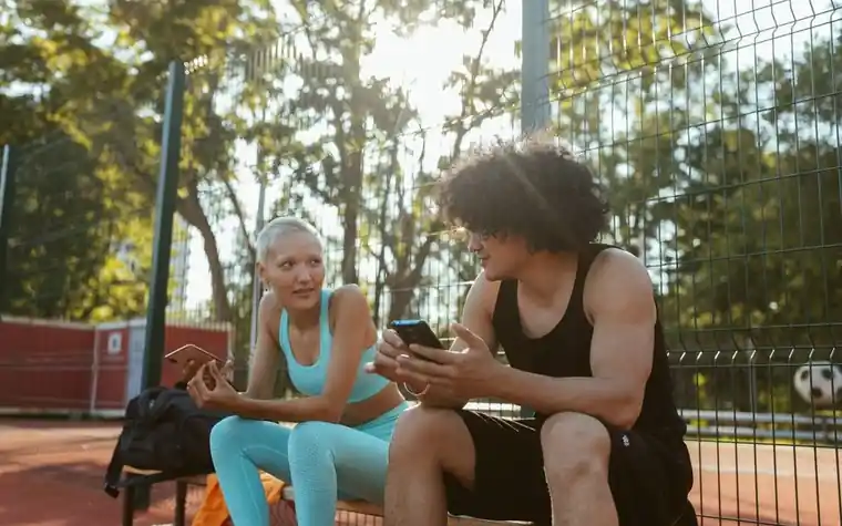 Two friends checking a smartphone together outdoors at a sports facility