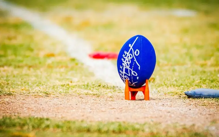 American football resting on an orange kicking tee on a grass field before a play