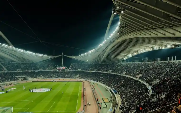 Packed stadium under floodlights viewed from the upper stand during a night soccer match