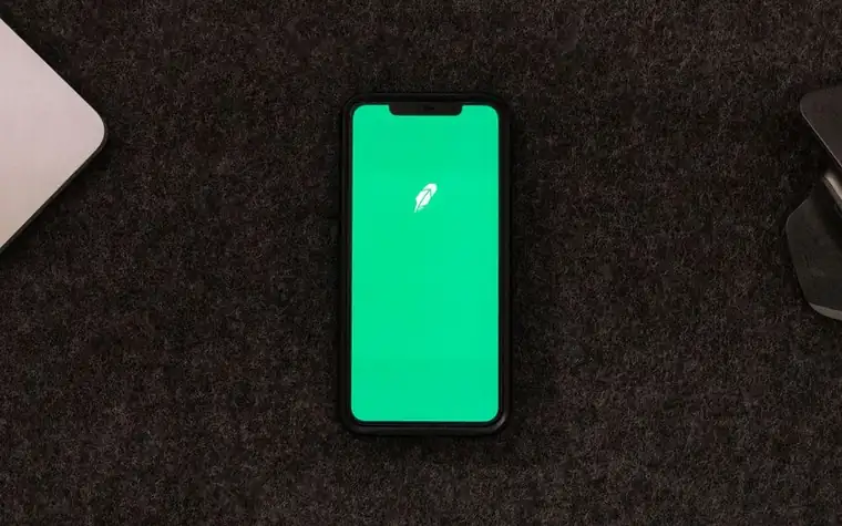 Smartphone lying on a wooden desk showing a green finance-style app screen