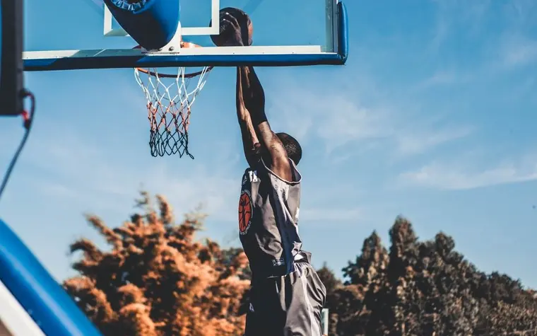 Basketball player elevating for a dunk on an outdoor court at dusk