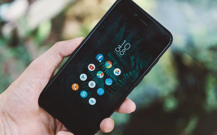 Hand holding a smartphone displaying a dark grid of app icons