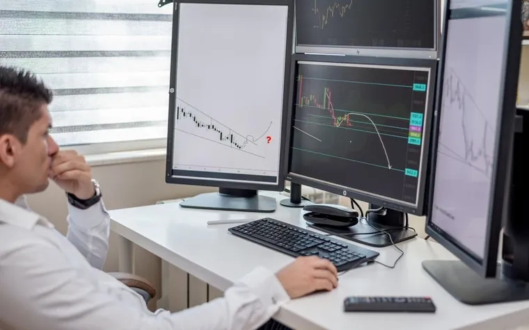 Analyst leaning on hand while watching multiple market charts on office monitors