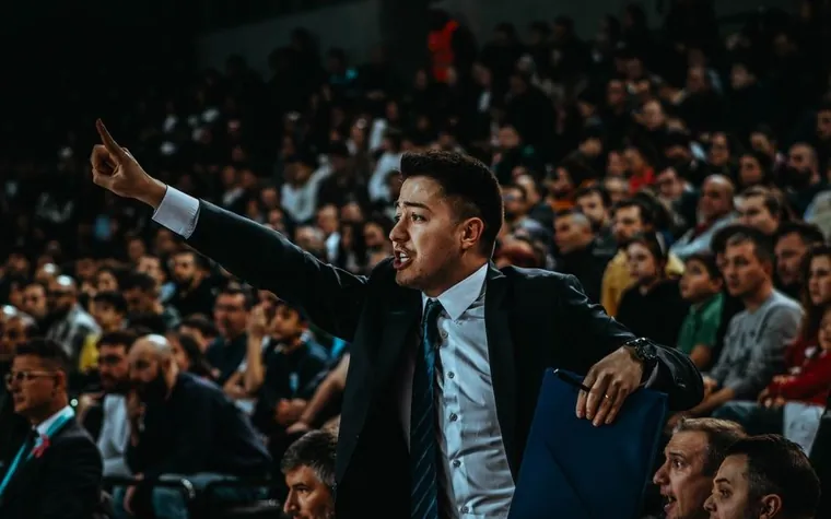 Coach gesturing courtside with a crowded arena behind him