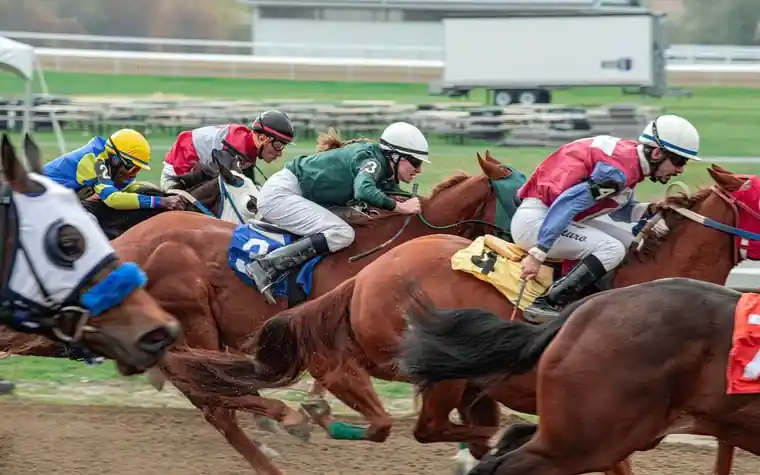 Jockeys in colorful silks racing a tight pack of horses down a dirt track