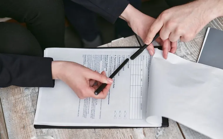 Close-up of two hands finalizing a signature with a pen on a paper document