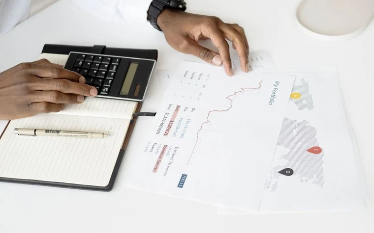 Overhead view of a hand holding a calculator beside financial charts and a notebook