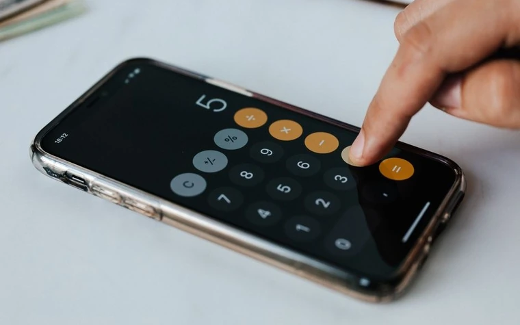 A finger pressing a percent button on a smartphone calculator app showing the number five