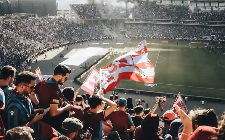 A packed stadium crowd waving red and white flags above the stands during a match