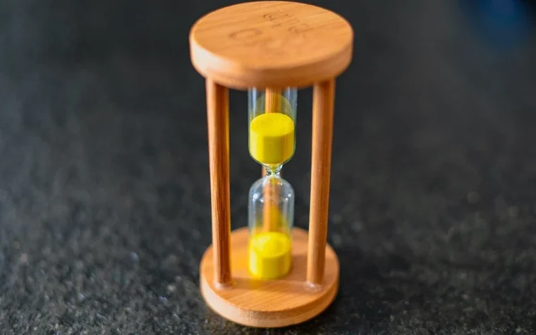 A wooden hourglass with yellow sand on a dark textured surface