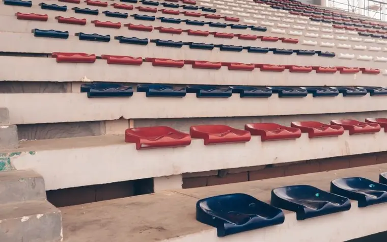 Rows of empty stadium bleacher seats in red, navy, and white plastic under daylight