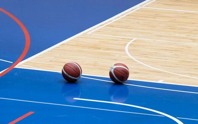 Two basketballs resting on the blue painted key of an indoor hardwood court