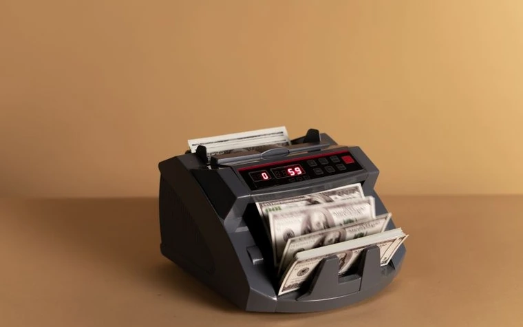 A countertop machine counting and sorting stacks of US dollar bills