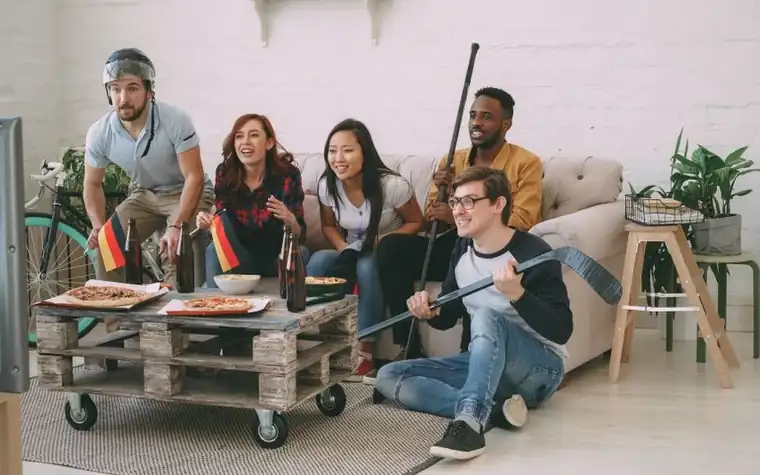 Group of friends cheering while watching a football game together on a living room television