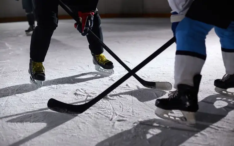 Two hockey players' sticks crossed while battling for the puck on the ice
