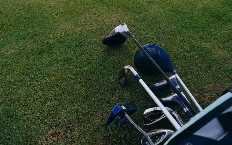Golf clubs and a driver head lying loose on cut grass beside an open golf bag
