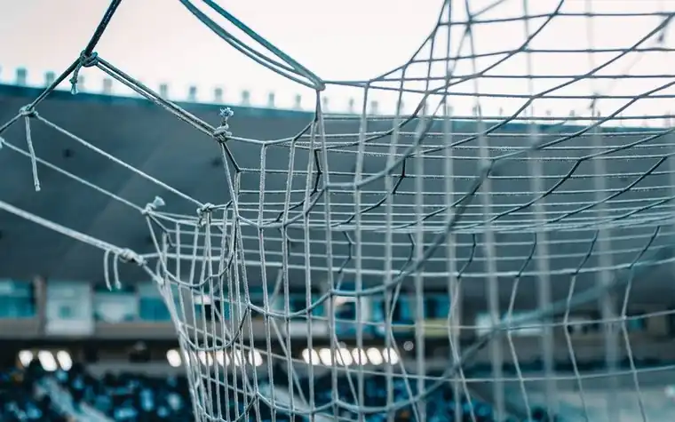 Close-up of a white soccer goal net with blurred stadium seating visible in the background