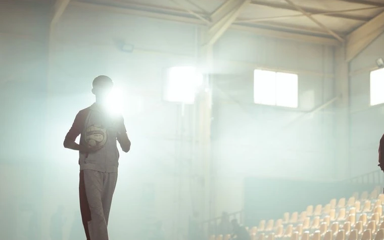 Silhouette of an athlete holding a ball standing in a hazy, backlit indoor sports arena