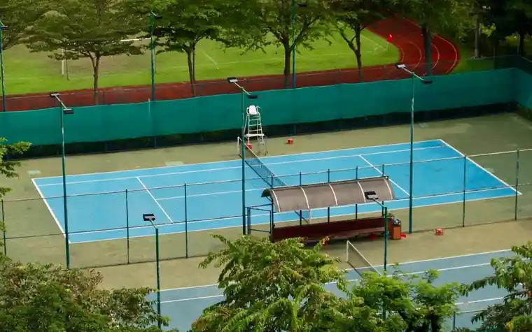 Empty blue tennis court seen from above with an umpire chair, players' bench, and a running track visible beyond the fence
