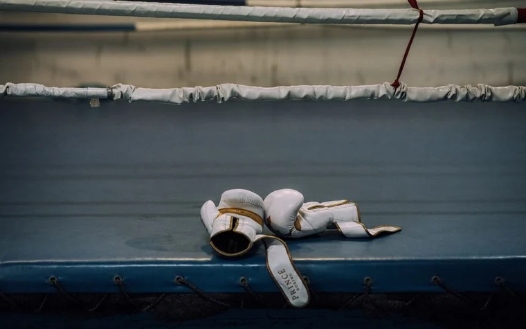 Pair of white boxing gloves resting on the canvas inside an empty boxing ring