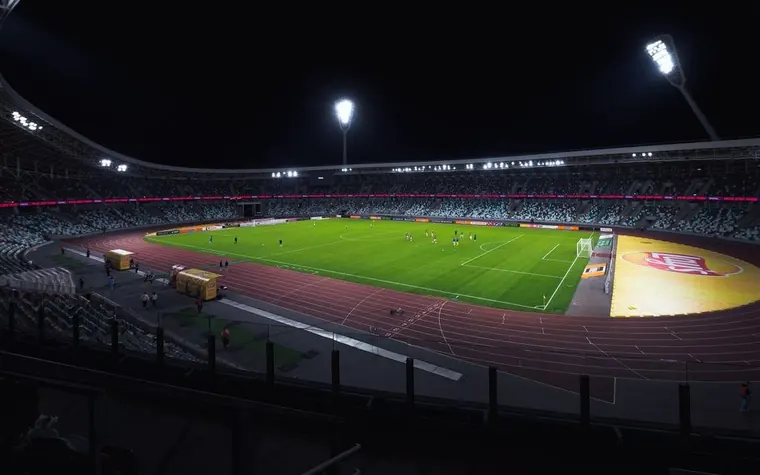 Floodlit soccer stadium at night with an empty green pitch and a running track around it
