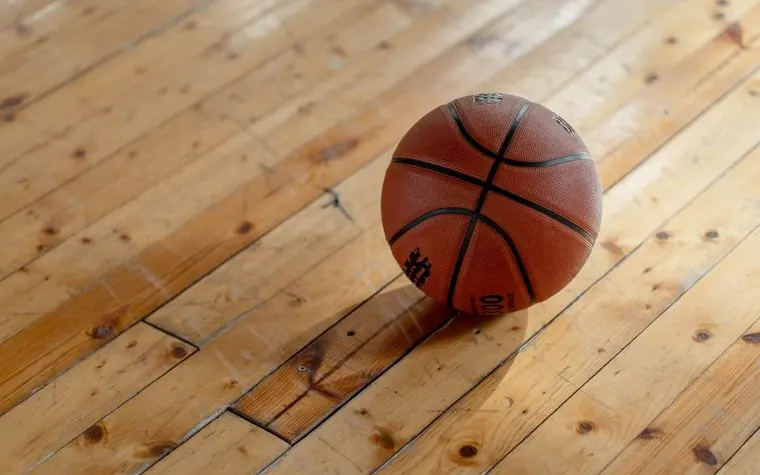 orange basketball resting on a scuffed wooden gym floor with the grain of the boards running diagonally