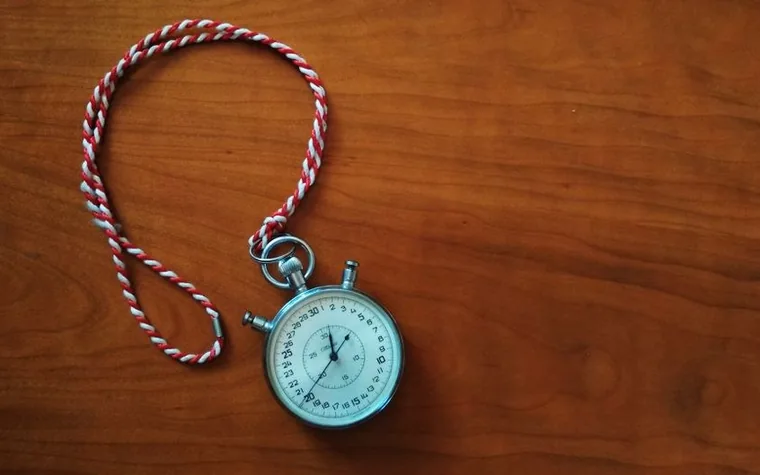 antique pocket stopwatch with a pale blue face and a red and white cord laid on a dark wooden table