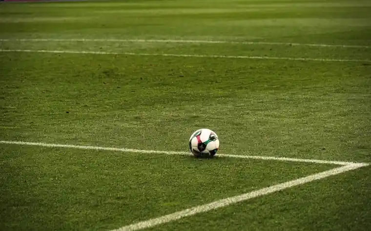 a white and black soccer ball resting on green grass at the corner where two white pitch lines meet