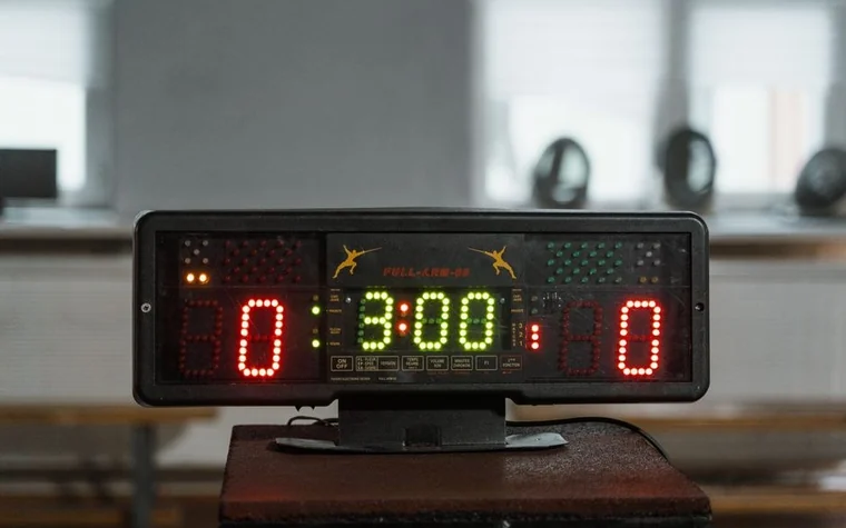 Electronic scoreboard showing a nil-nil score and a three-minute countdown clock in an empty indoor sports hall