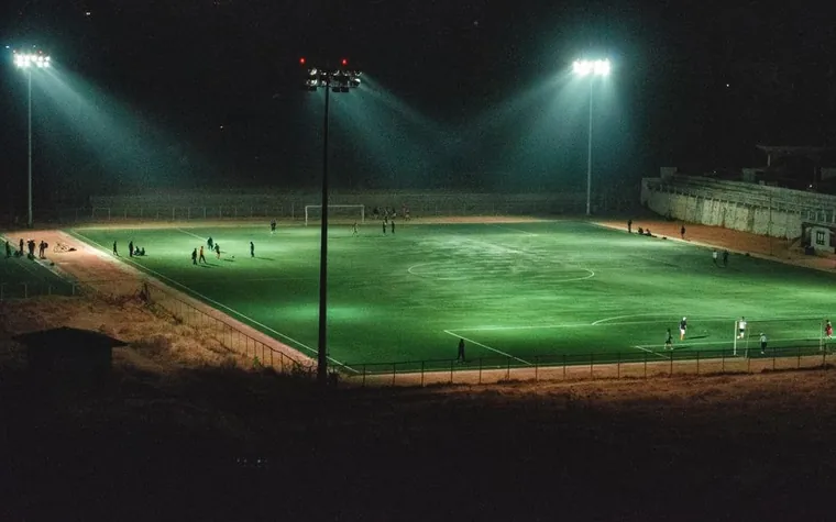 Floodlight towers lighting a green football pitch at night with players spread across the field