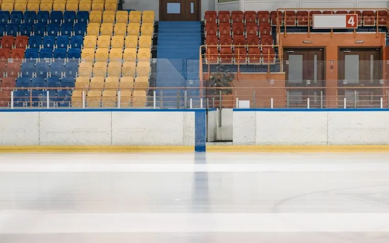Empty ice rink boards with yellow, blue and red arena seats and a gate marked number four behind them