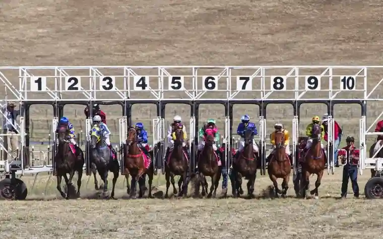 Numbered starting gates one through ten at a horse racing track with jockeys and horses bursting out at the break