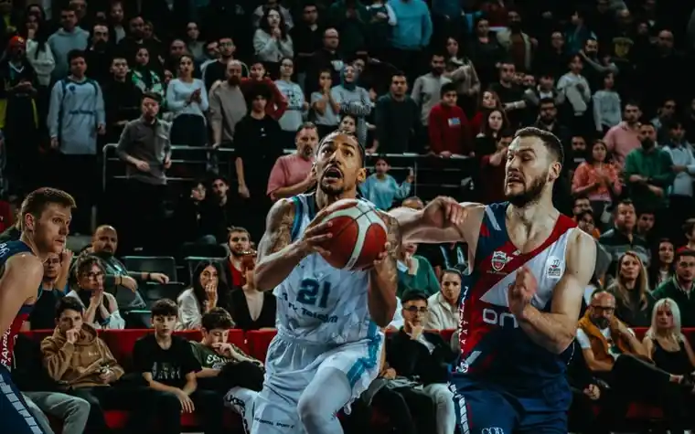 Two basketball players battling for a rebound in front of a packed, cheering arena crowd