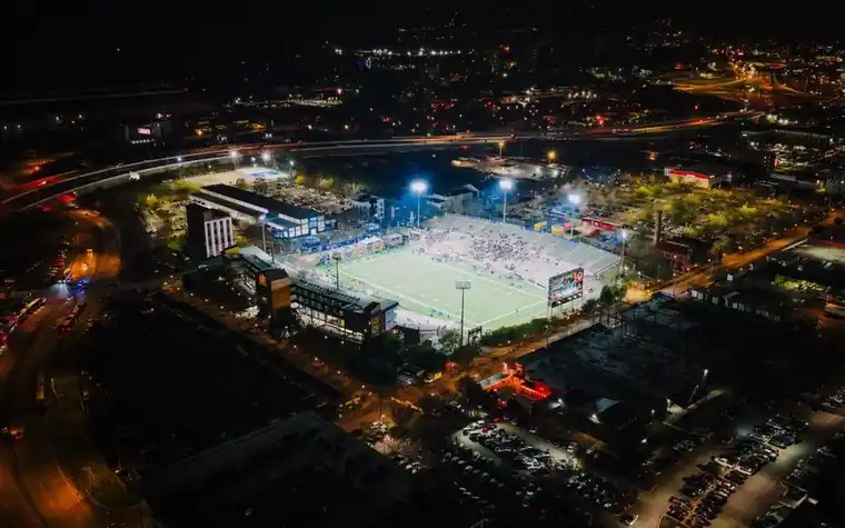 Aerial night view of a brightly lit outdoor stadium surrounded by a dark city skyline