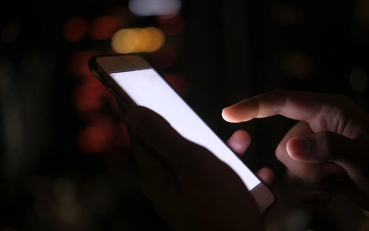 Close-up of a hand tapping a smartphone screen in the dark with blurred city lights in the background