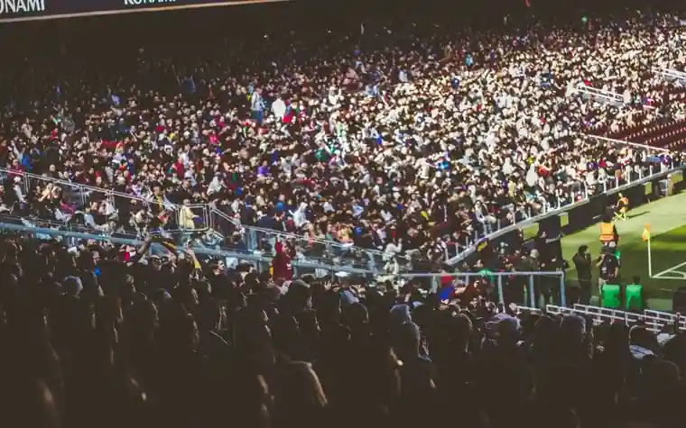 Densely packed stadium stands filled with fans watching a floodlit night match