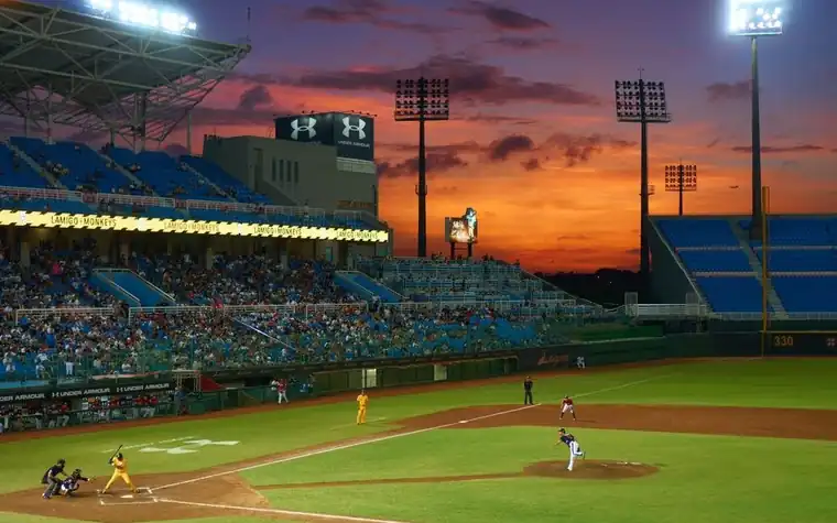 Baseball game in progress on a stadium field under a vivid orange sunset sky