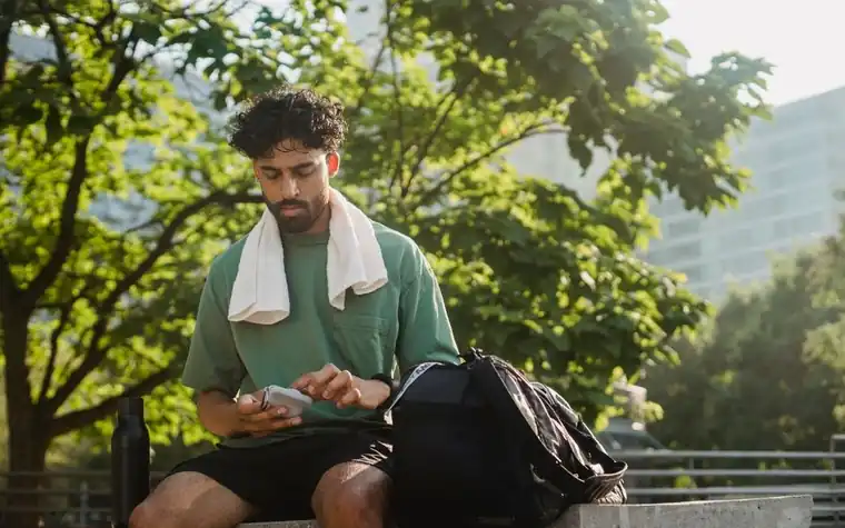 Man sitting outdoors checking a smartphone screen before placing a wager online