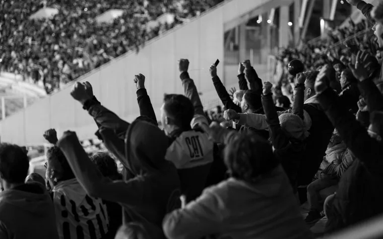 Black and white photo of a crowd with fists raised cheering in a stadium