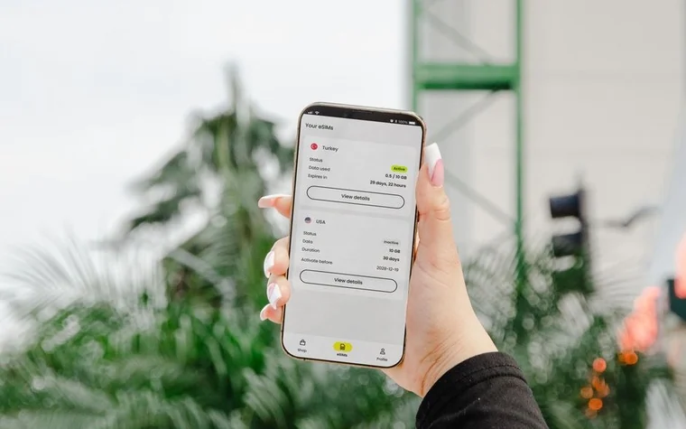 Hand holding a smartphone showing an app screen outdoors with a blurred traffic light in the background