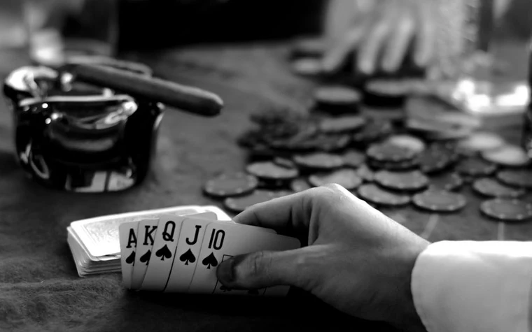 Hand holding a straight of ace, king, queen, and jack playing cards beside stacked casino chips