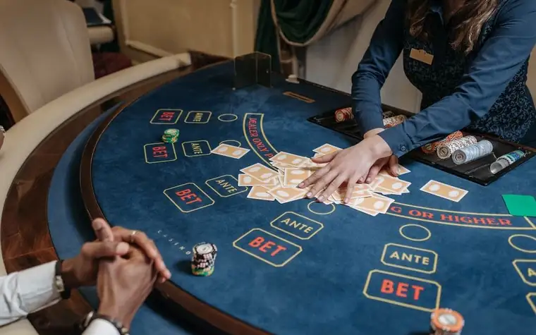 Casino dealer shuffling cards on a felt gaming table marked with ante and bet betting spots