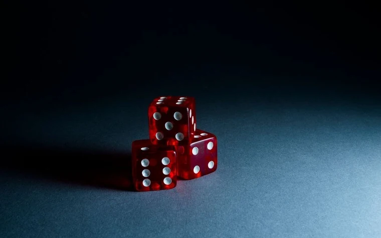 Three red dice stacked together on a dark casino table surface