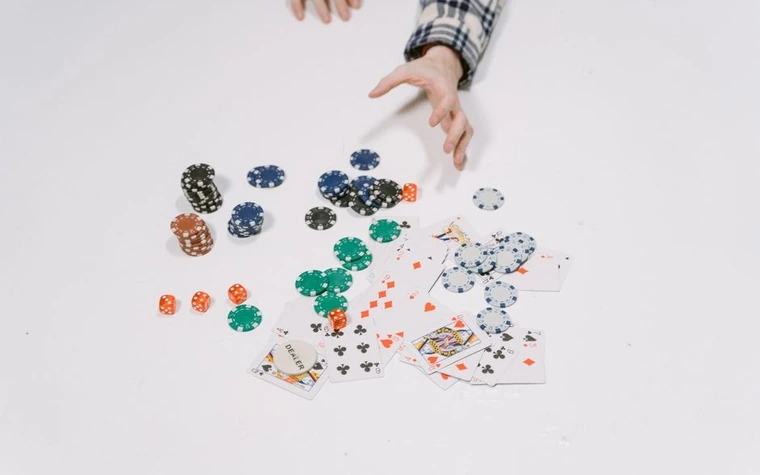 Casino chips, dice, and playing cards scattered across a white surface with a hand reaching toward them