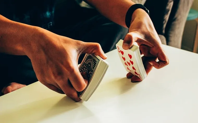 A pair of hands shuffling a deck of playing cards using the riffle technique on a white table