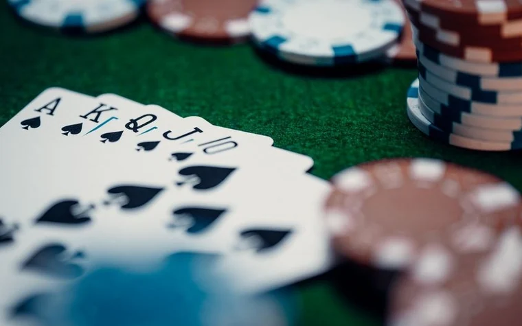 A royal flush of spades, Ace through Ten, fanned on green felt beside stacks of poker chips