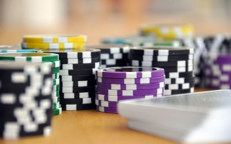 Tall stacks of black, purple, yellow, and green poker chips next to a deck of playing cards on a wooden table