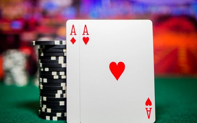 Two aces, diamonds and hearts, standing upright in front of a stack of black chips on green felt